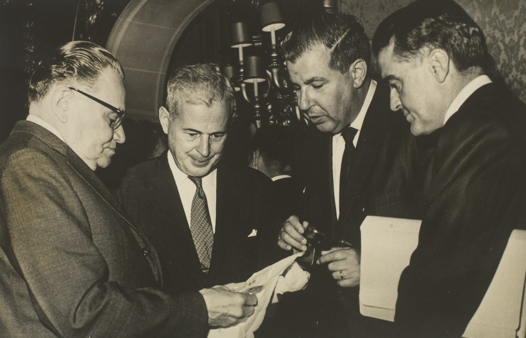 Three men in suits looking at a piece of paper.